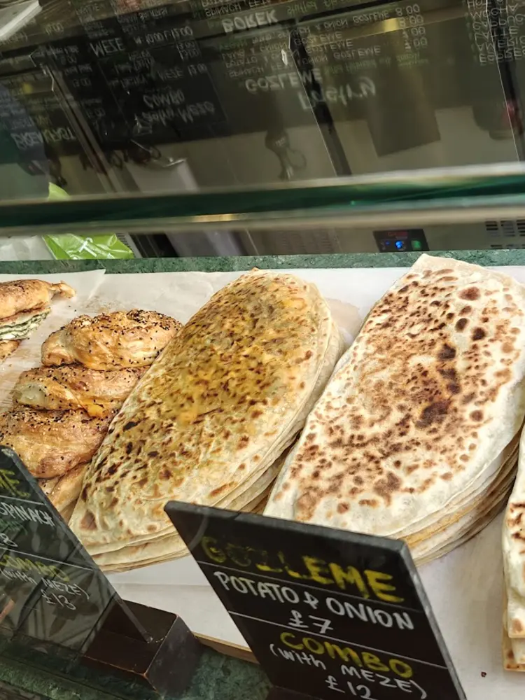 Counter display of folded gözleme and coiled spinach börek beside chalk price boards