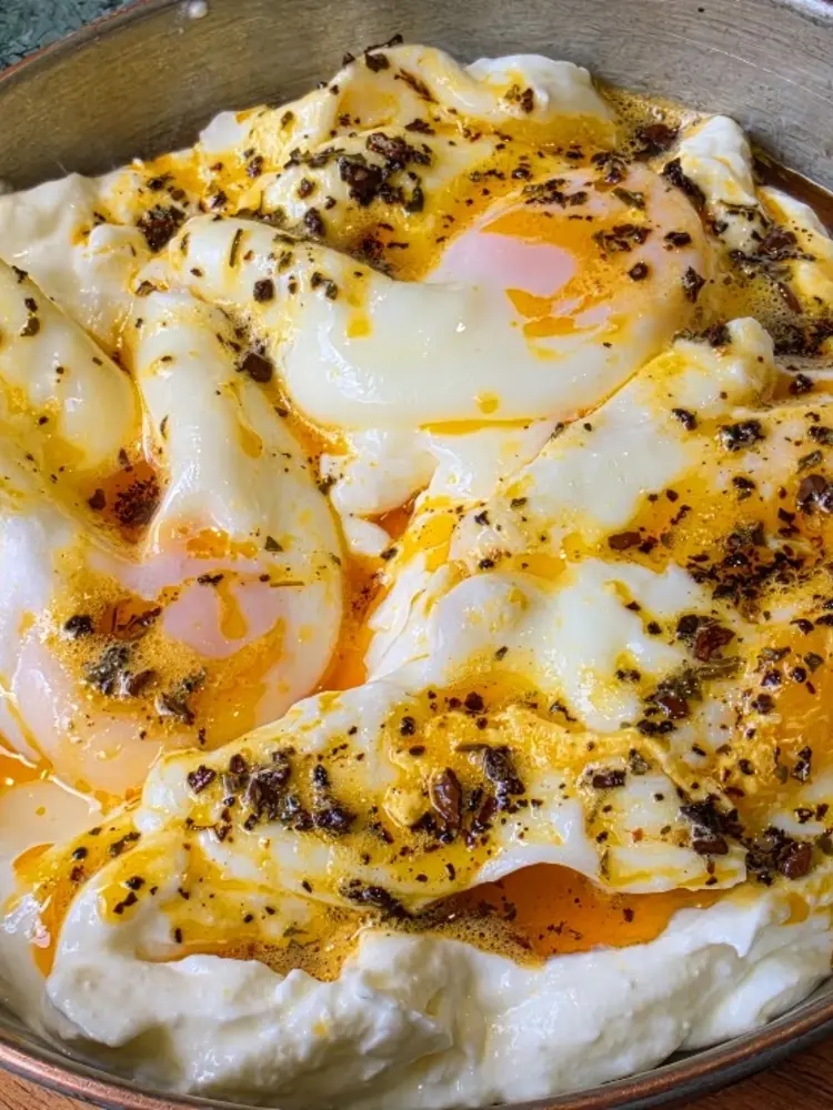 Poached eggs on garlic yoghurt with chilli butter in a copper pan on a wooden board